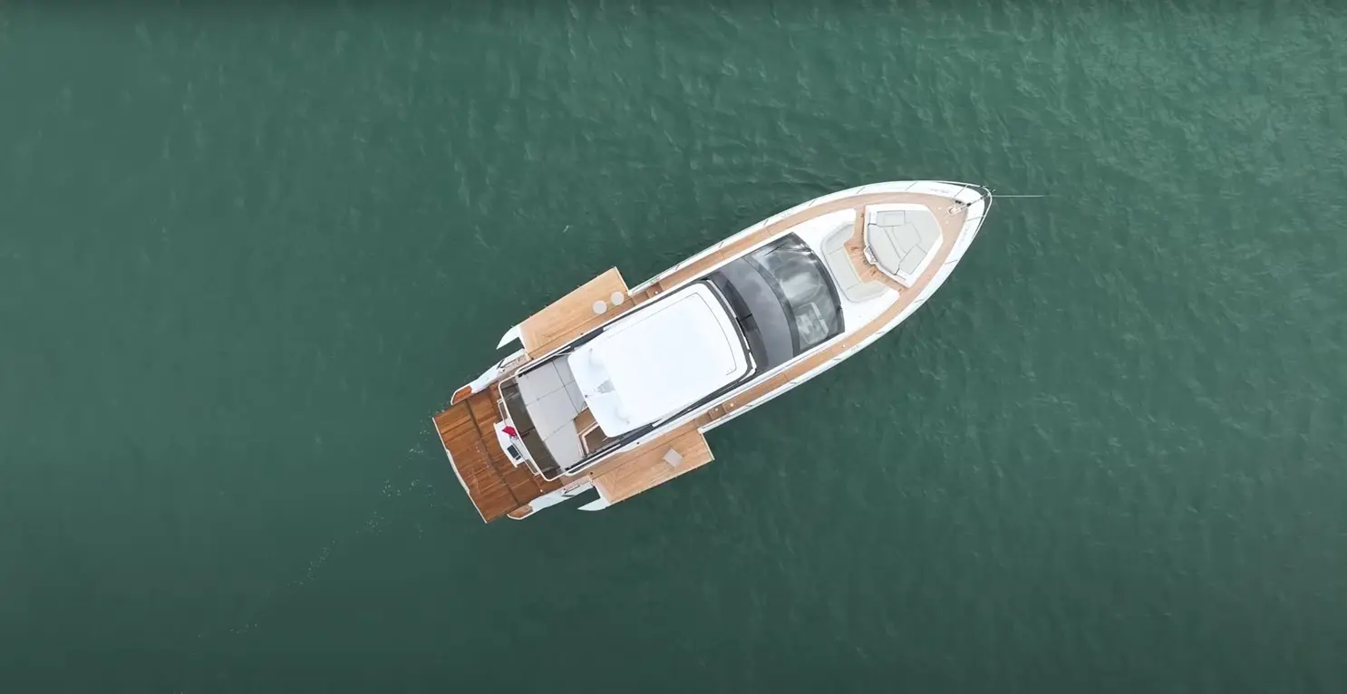 An aerial view of a sleek motor yacht with a wooden deck, floating on calm turquoise waters.